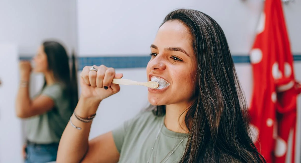 Young woman brushing teeth with toothbrush in a modern, bright bathroom. Focus on oral health care and hygiene.