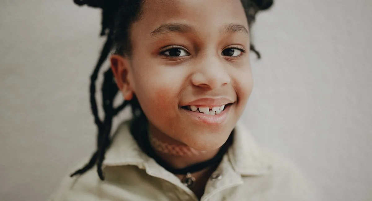 Close-up headshot of a smiling child with afro pigtails and a playful expression.