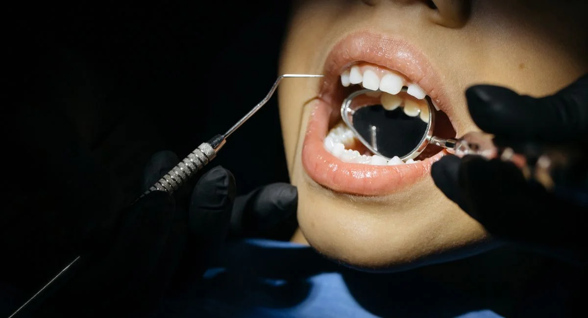 A close-up view of a child undergoing a dental examination with tools in their mouth.