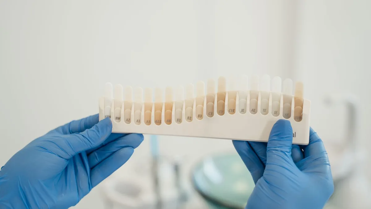 Des mains gantées présentent un nuancier de teintes dentaires