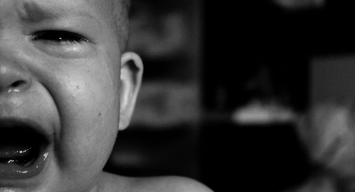 Emotional close-up of a crying baby's face captured in black and white with a blurred background.