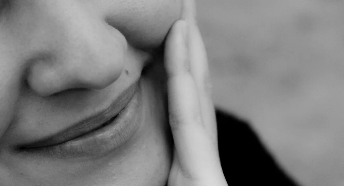 Close-up black and white photo of a smiling woman with hand on cheek.