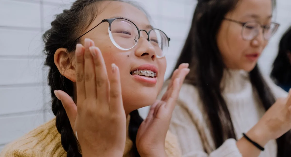 Cheerful teenage girl with glasses and braces smiling indoors, embracing joy and positivity.