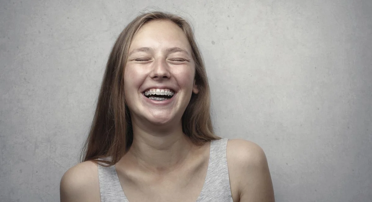 A cheerful woman with braces laughing joyfully in a casual portrait.