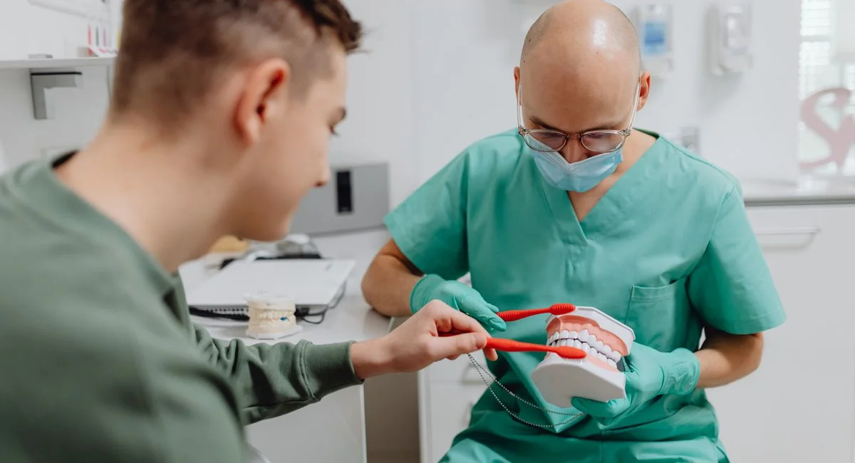 Dentist demonstrating proper brushing technique to patient using dental model.