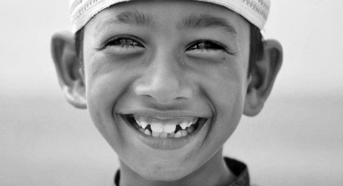 A joyful portrait of a child with a wide smile and traditional headwear.