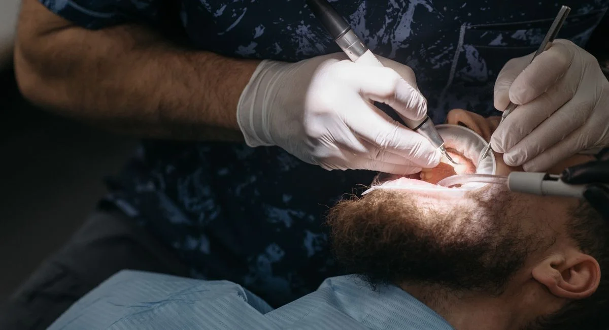 Dentist using tools for dental examination on a bearded male patient.
