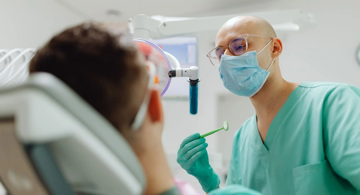Dentist examining a patient's teeth with focus on tools in a well-lit clinic.
