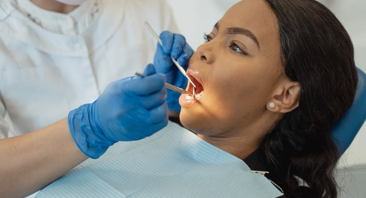 A female patient undergoing a dental checkup by a healthcare professional wearing gloves and a facemask.