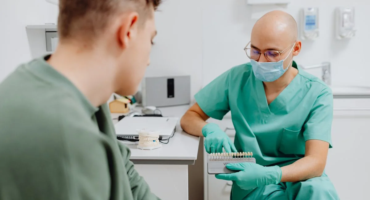 Dentist in scrubs showing a shade guide to patient for dental evaluation.