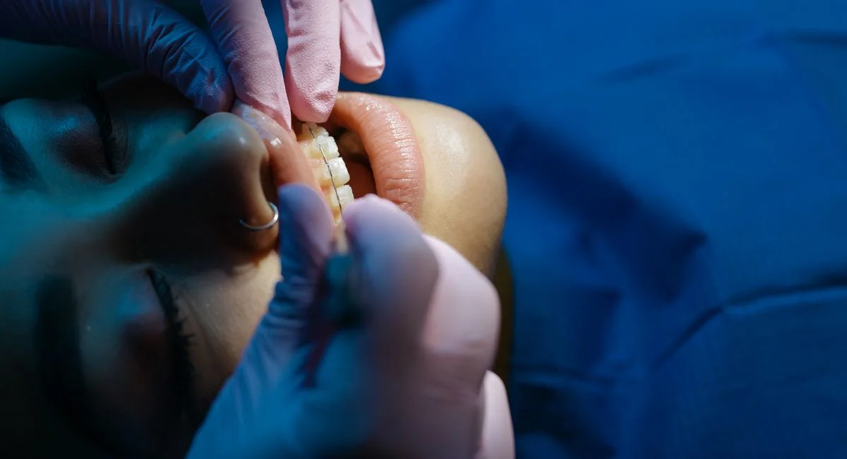 A dentist examines a patient's teeth during a dental procedure under bright clinic lights.