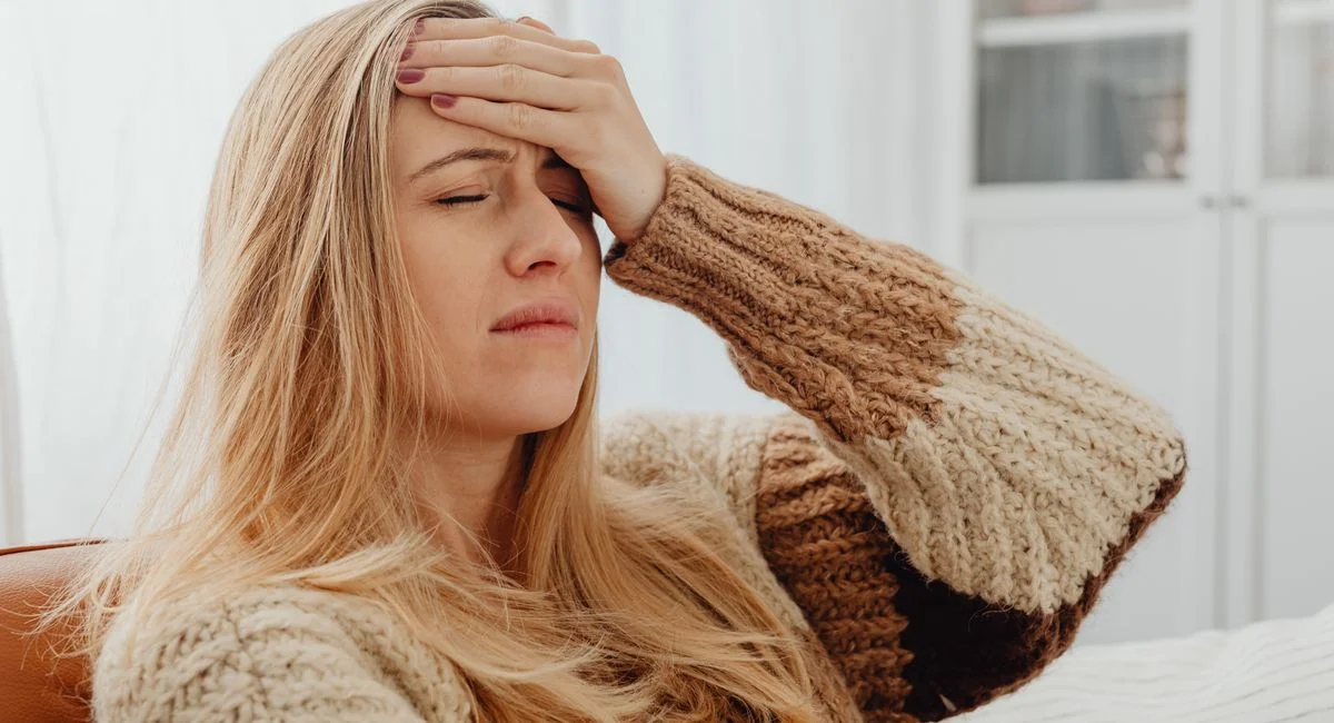 Close-up of a woman with a headache, hand on forehead, in a comfortable setting.