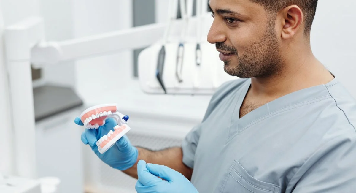 Dentist wearing scrubs and gloves demonstrates dental care with a teeth model.