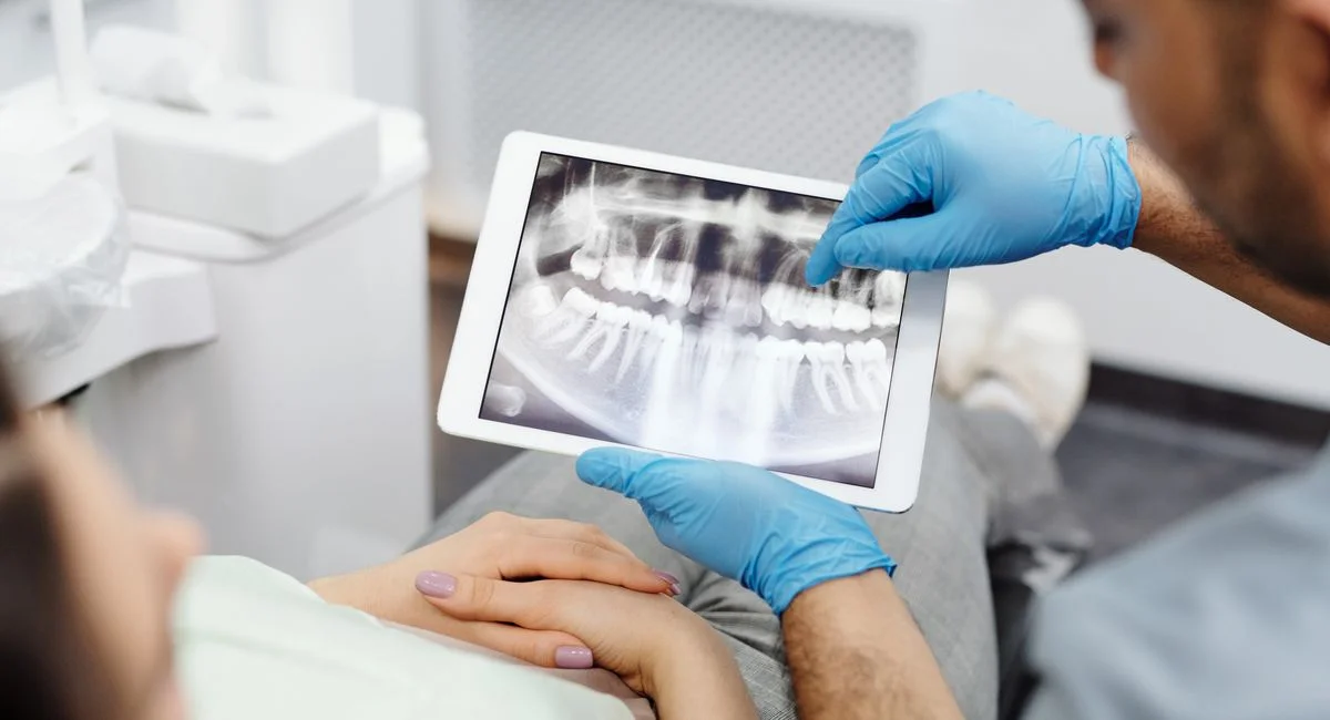 Dentist reviewing a dental X-ray with a patient using a tablet, highlighting modern dental care.